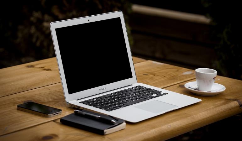 Laptop op tafel met notitieboekje, mobieltje en kopje thee